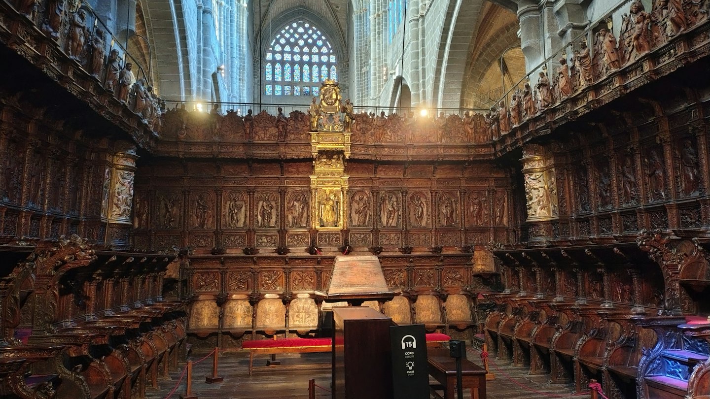 Stalli lignei intagliati di una cattedrale sotto una finestra ad arco con vetrate.