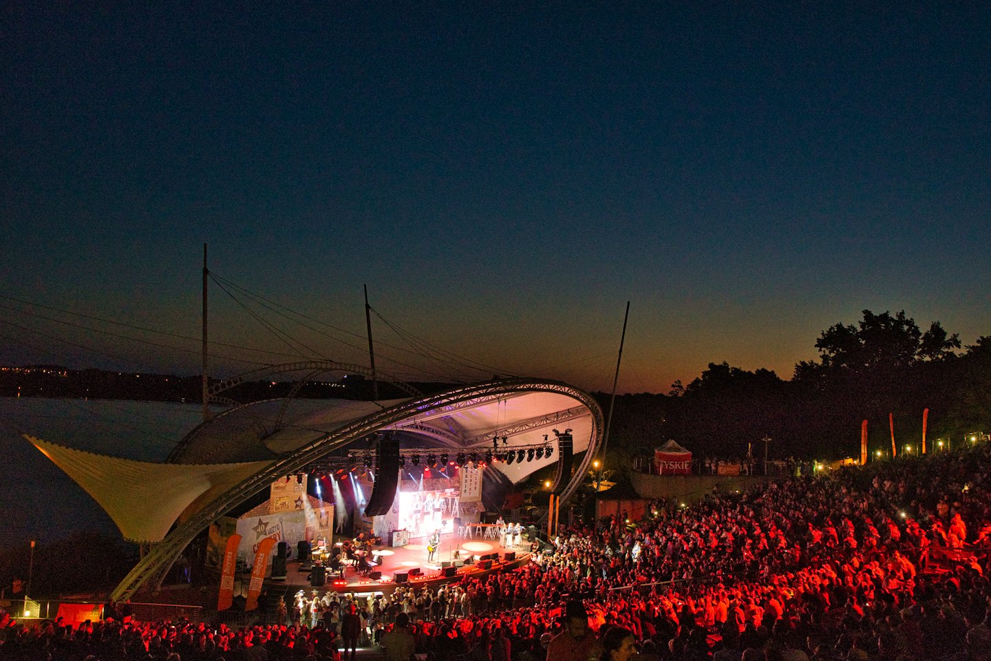 Una grande band si esibisce su un palco all'aperto per un pubblico su una collina.