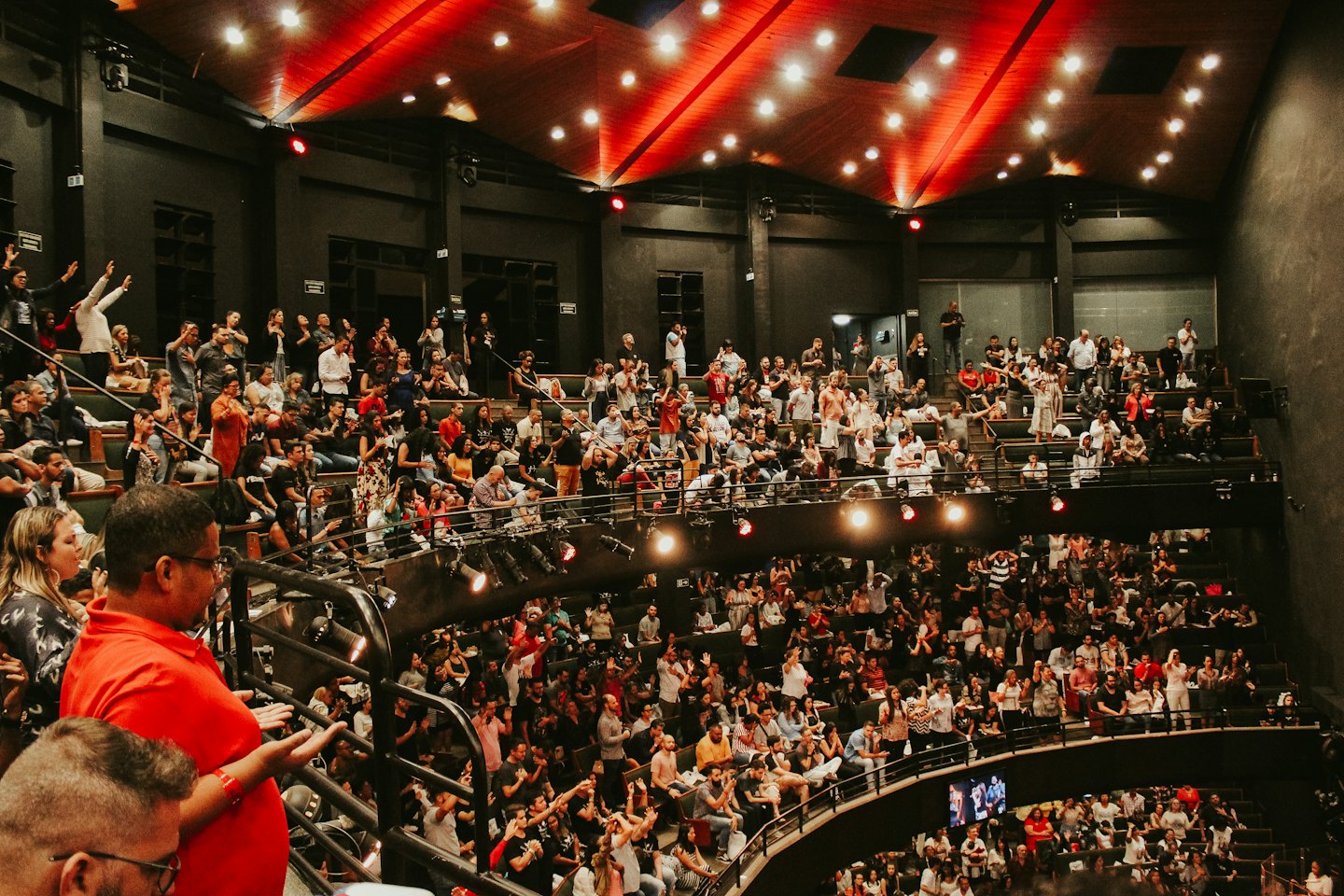 Un pubblico entusiasta in piedi applaude all'interno di un grande auditorium.